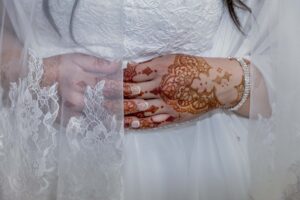Close up shot of a bride in a white lace wedding gown and lace veil. Her hands, intricately decorated in henna, are folded over her midsection for her Middle Eastern wedding.